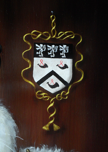 The Hinksman coat of arms, surrounded by a golden ribbon that ends with golden tassels, suspended by a small black nail. Devices were used a lot in paintings to allow something abstract, such as the coat of arms, to exist within the boundary of the painting where everything else has to conform to the restrictions of 'being real.' Copyright (c)2016 Paul Alan Grosse